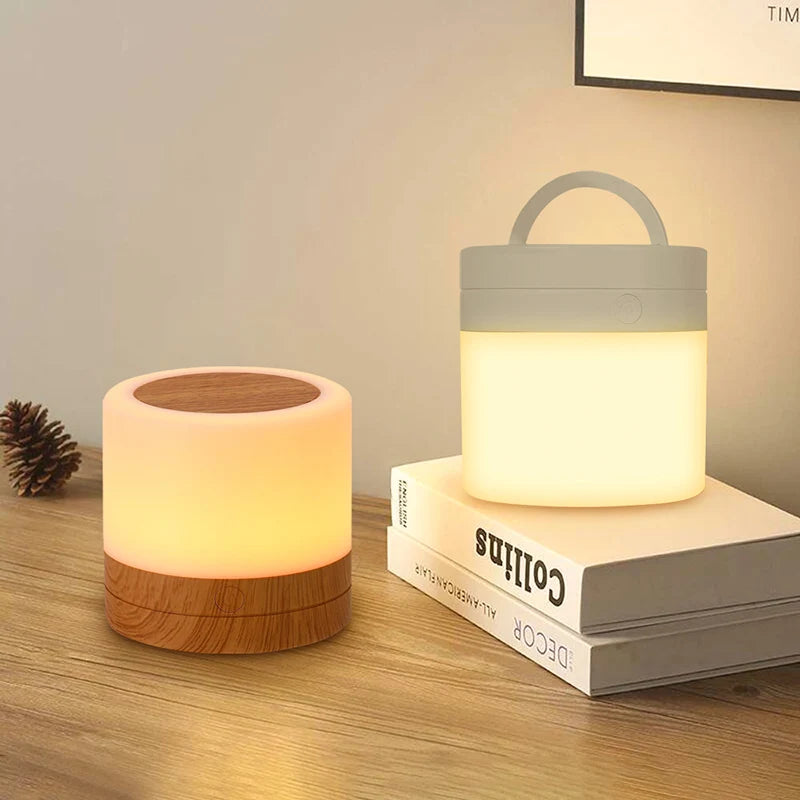 Luminária para quarto Aura 360 com base amadeirada e base branca emitindo luz quente suave em cima de uma mesa com livros.