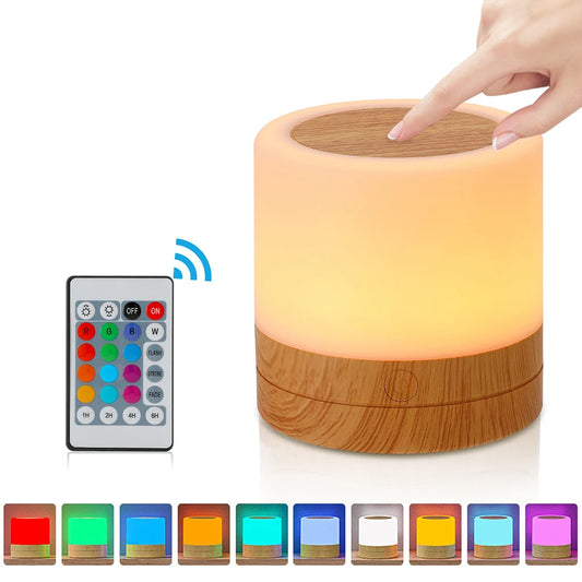 Luminária para quarto Aura 360 com base amadeirada emitindo luz quente suave em diversas cores e controle no fundo branco. 