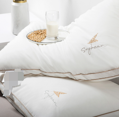 Travesseiro ortopédico Sillencia SoySoft branco com bordado Soybean e detalhes em linha dourada com um prato equilibrado em cima mostrando a qualidade do produto.