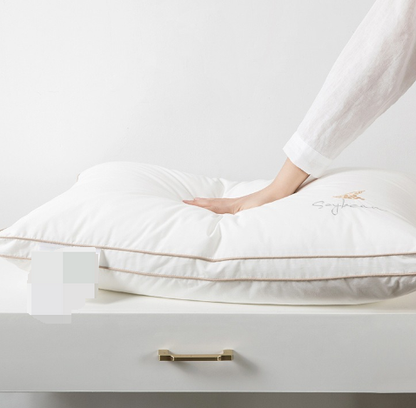 Travesseiro ortopédico Sillencia SoySoft branco com bordado Soybean e detalhes em linha dourada com uma mão mostrando a qualidade do produto.